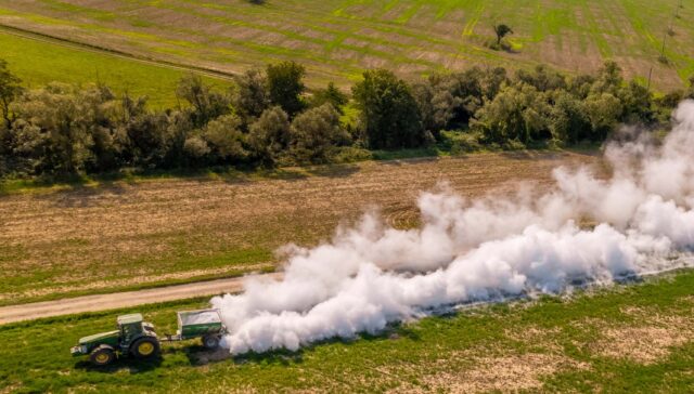 Aerial view of a tractor spreading lime on agricultural fields to improve soil quality after the autumn harvest. The use of lime powder to neutralize the acidity of the soil. Agricultural banner.